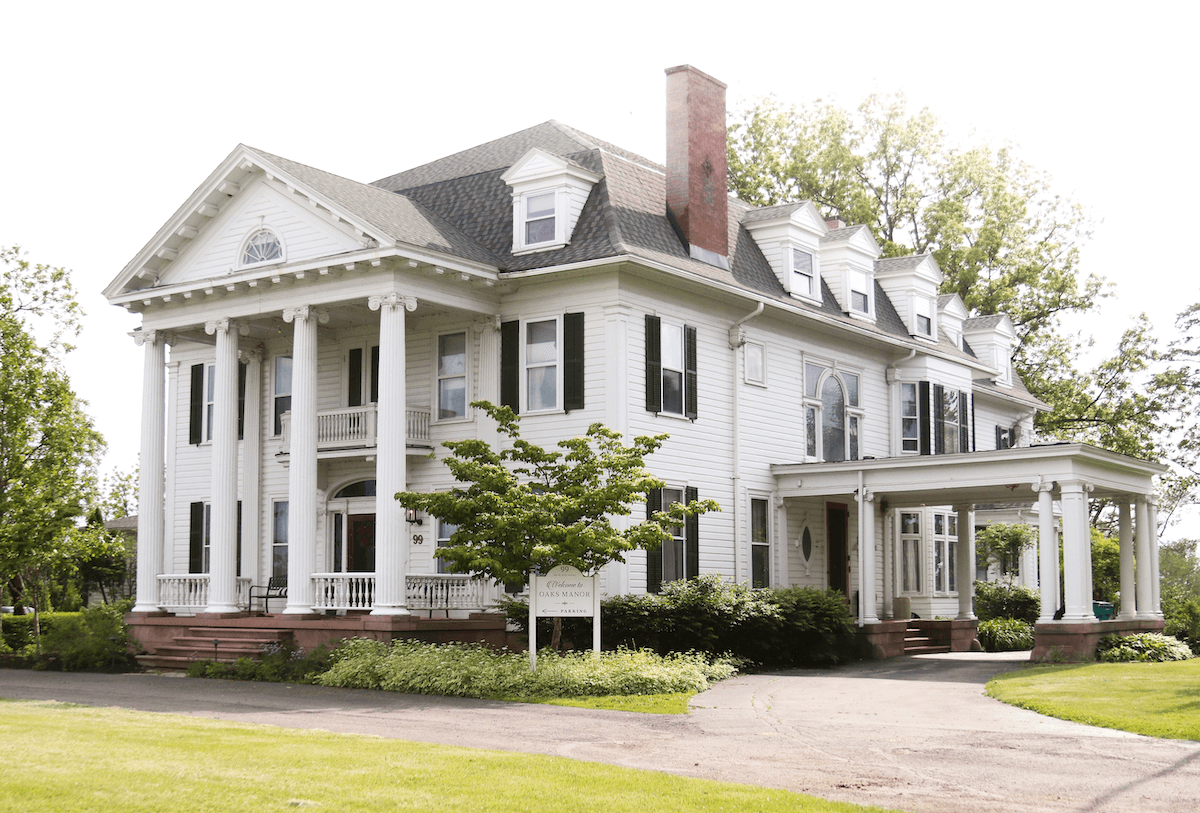 A large white mansion with columns and a balcony. The house has a brick chimney and a well-manicured lawn.