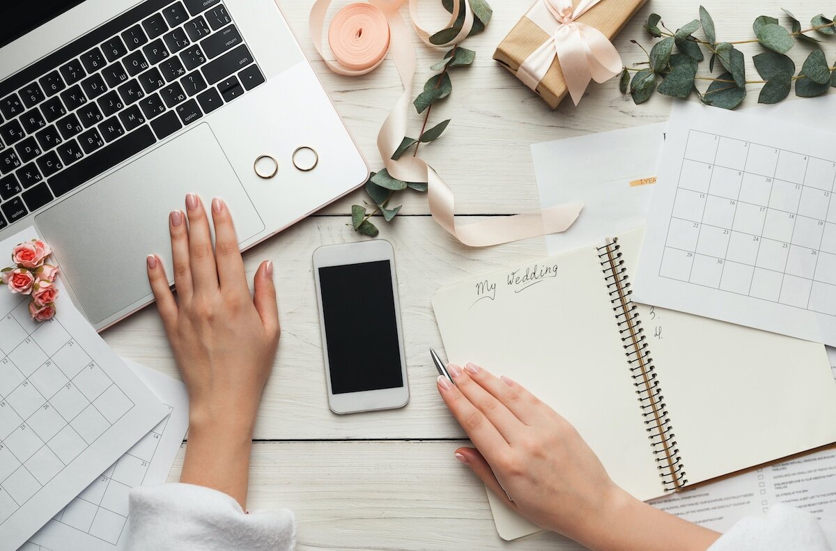 A person's hands on a desk with a laptop and notebook. The desk is organized with office supplies.
