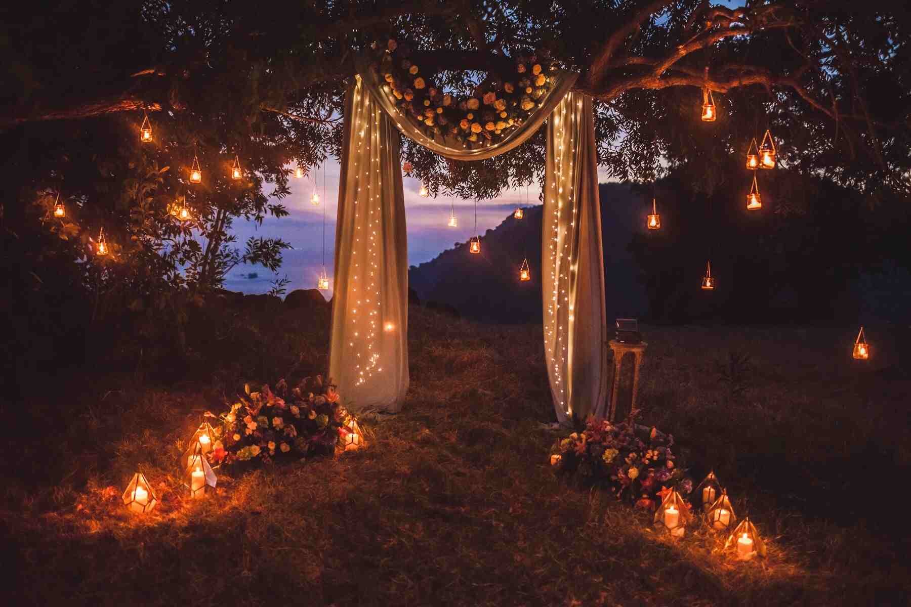 A beautiful wedding arch decorated with lights and flowers. Romantic outdoor wedding setup at dusk.