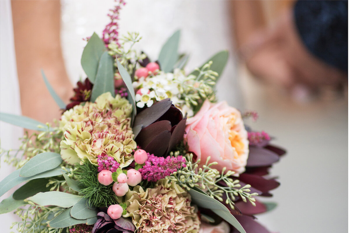A beautiful wedding bouquet with pink and purple flowers. The bouquet is made of a variety of flowers and greenery.