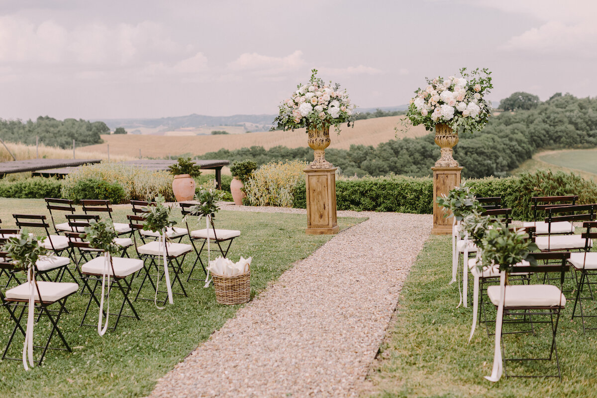 A serene wedding aisle with white chairs and beautiful floral arrangements on either side.