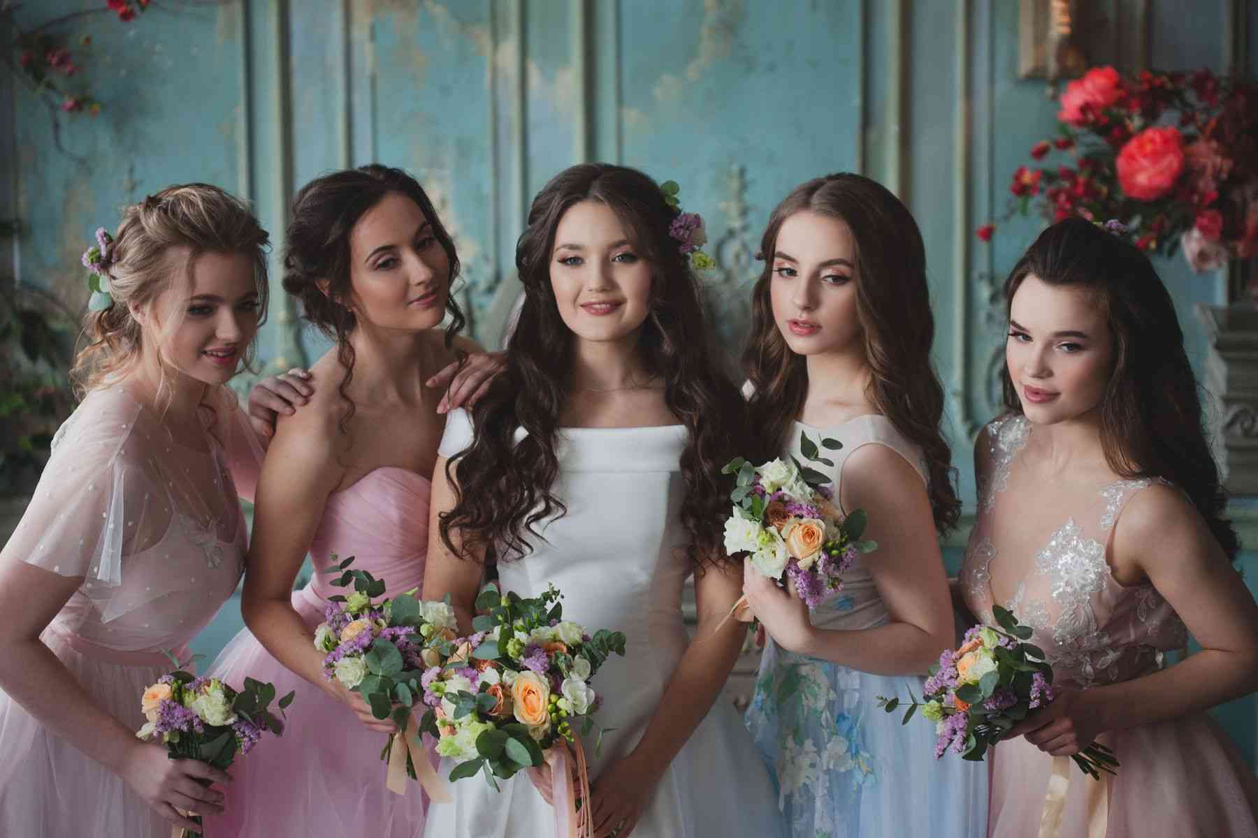 Group of bridesmaids with flowers posing together. Beautiful women in elegant dresses.