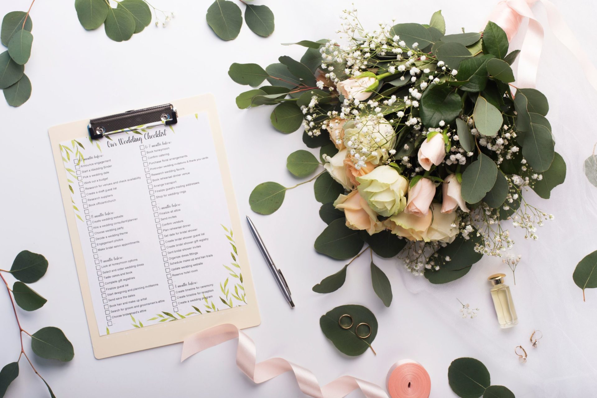 A wedding planning checklist on a clipboard with a bouquet of flowers, a pen, and ribbon.