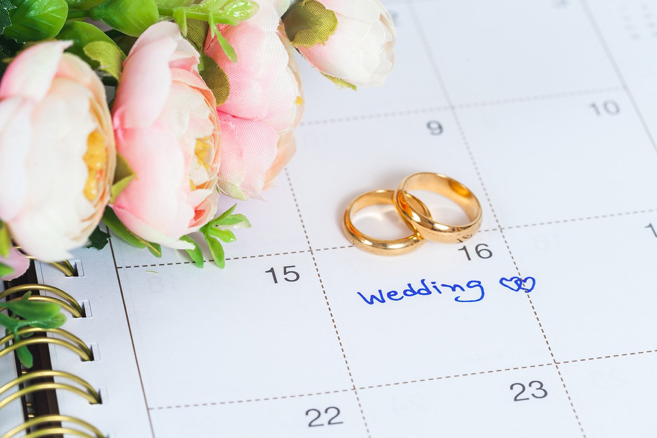Wedding planning calendar with golden rings and flowers. Upcoming wedding date marked.