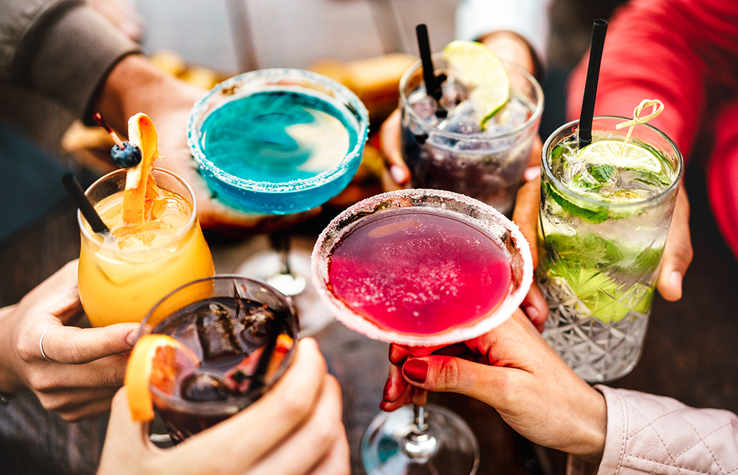 A group of people enjoying colorful cocktails together. Various drinks with straws are visible.