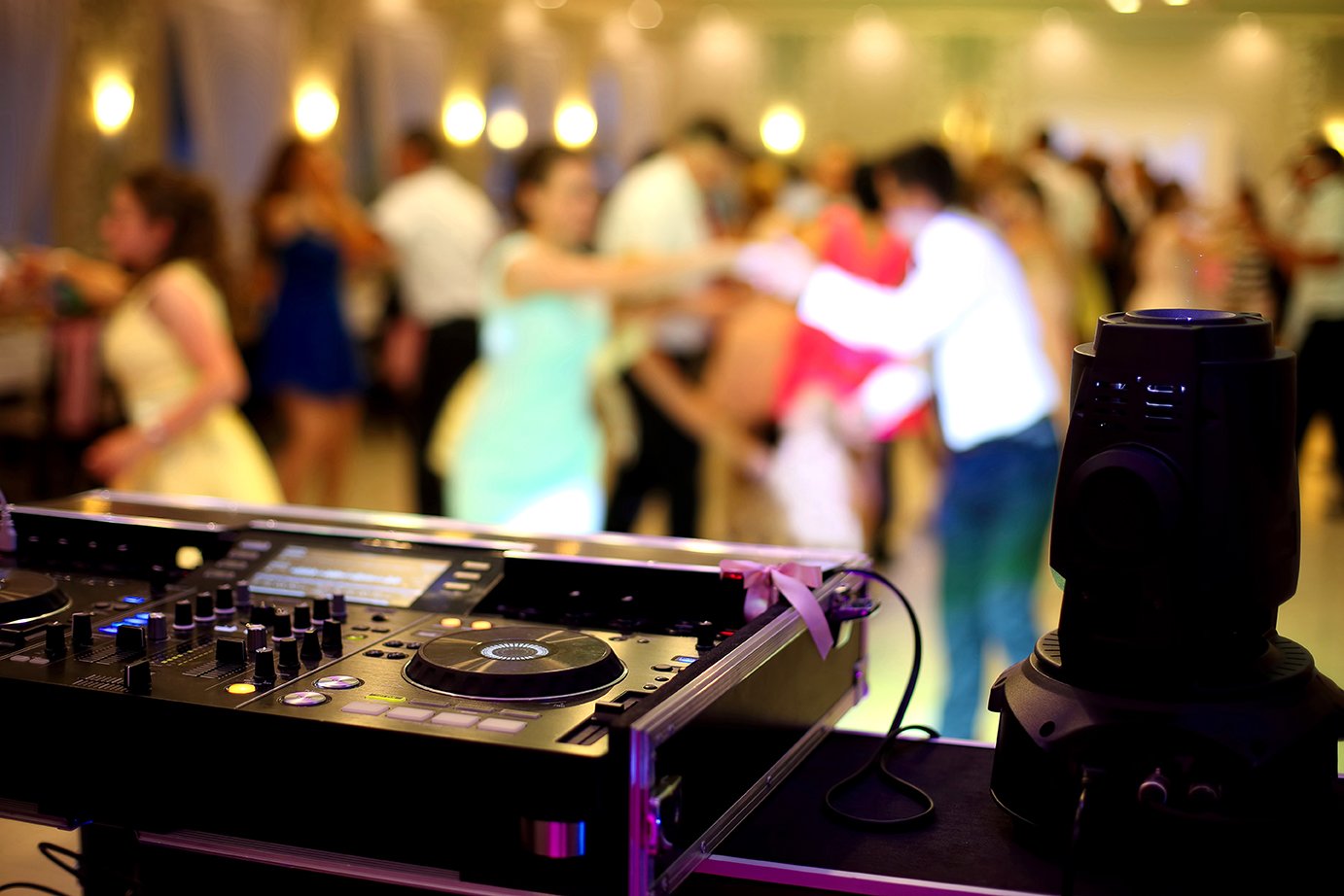 DJ setup with turntables and mixer. People dancing in the background.