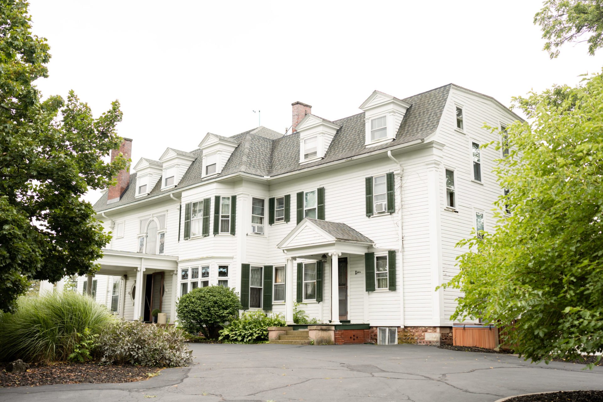 A large white house with green shutters and a driveway. The house has a gray roof.