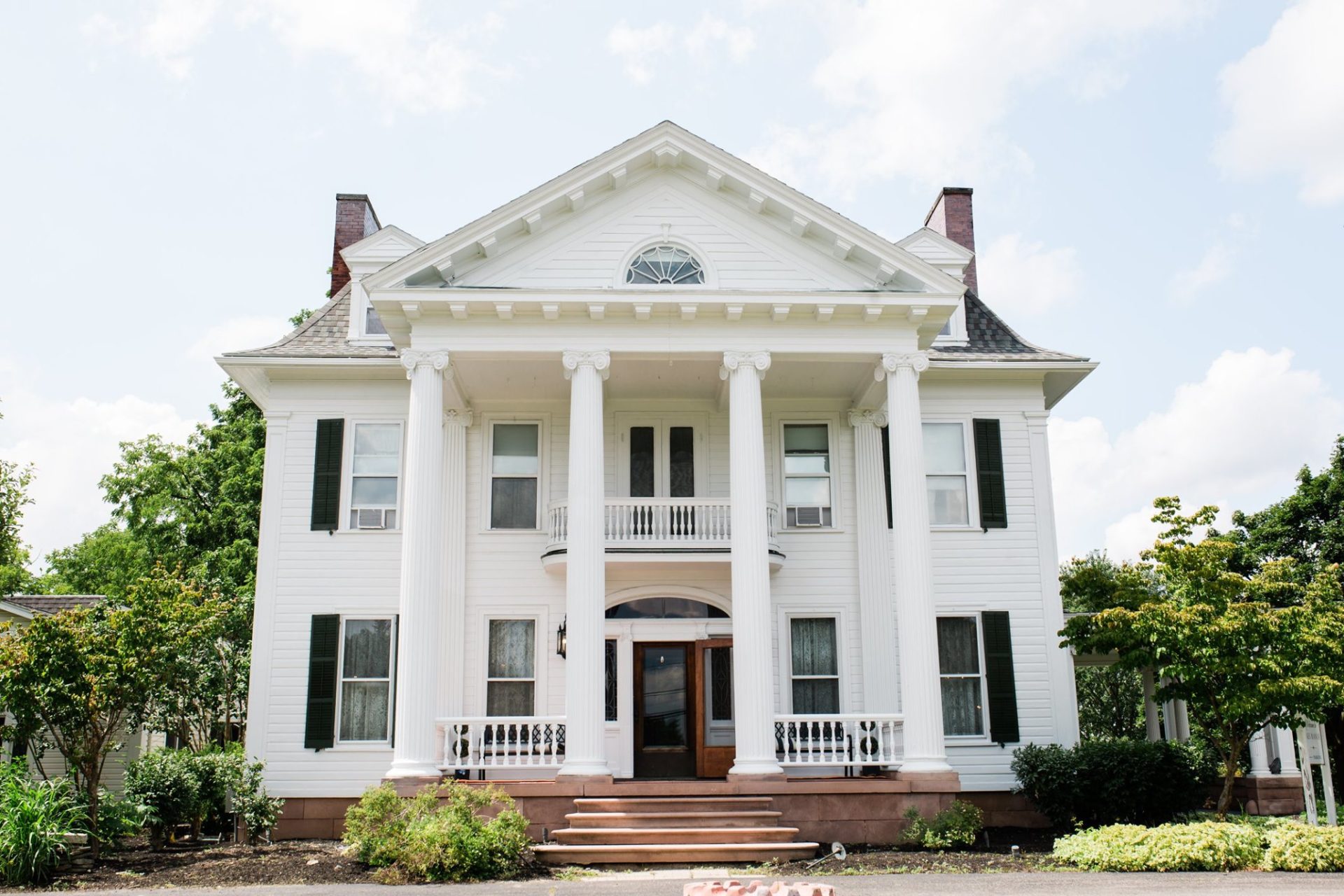 A large white house with columns and a balcony. The house has a classic southern style.