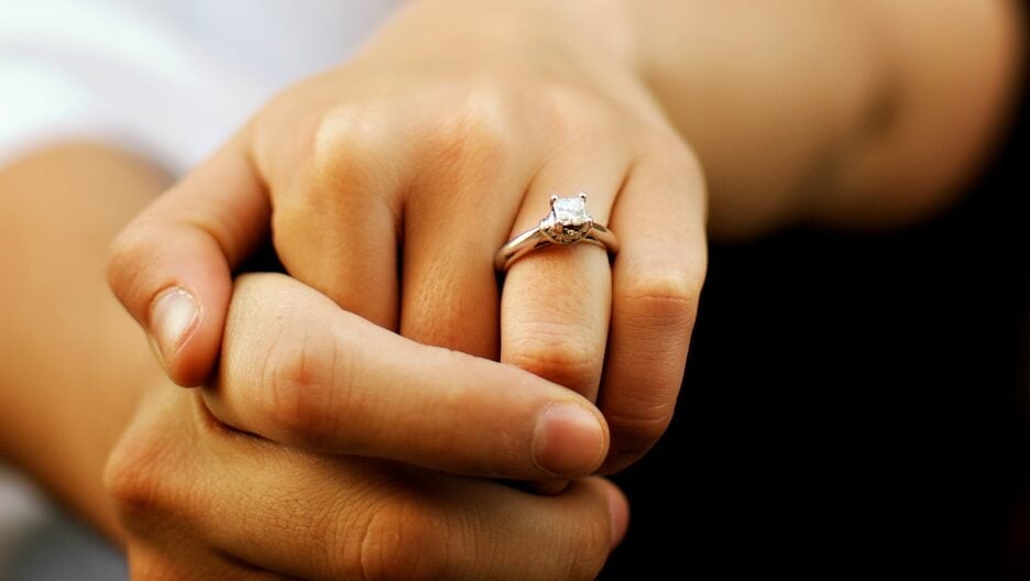 Interlocked fingers with a diamond ring on the finger. A symbol of love and commitment.