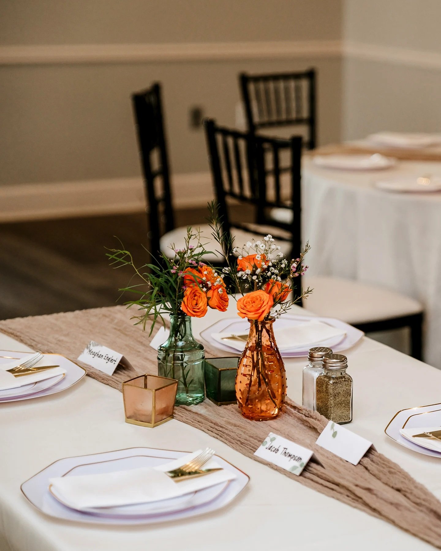 Elegant Wedding Table Setting with Flowers A beautifully set table with white plates, orange flowers, and candles. The table is decorated with a beige runner.