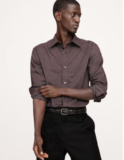 A man in a patterned shirt and jeans standing confidently. He appears to be in a dark room.