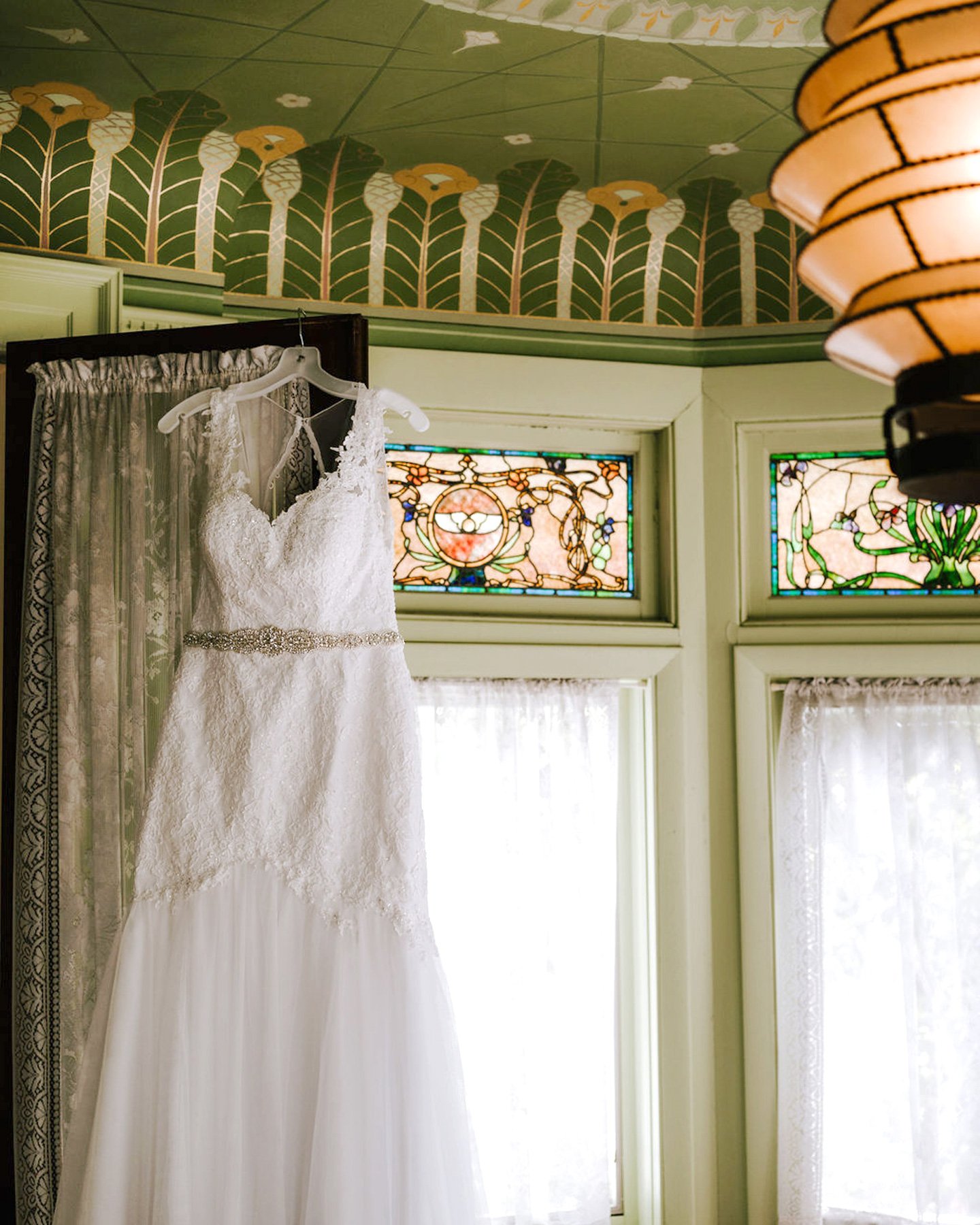 Elegant white wedding dress hanging by window A beautiful white wedding dress. Wedding dress hanging by the window.