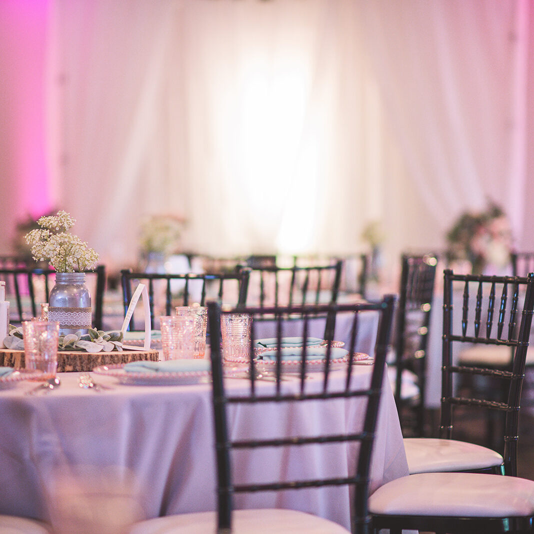 Elegant Wedding Reception with Pink Uplighting A beautifully set table with black chairs and pink lighting. The room is set for a formal event.
