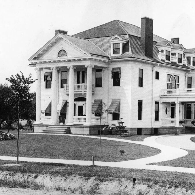 Large White Mansion with Columns and Chimney A large white mansion with columns and a chimney. The building has multiple stories and a large front yard.